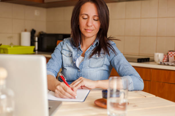 istock Mid adult woman taking notes while working at home. 1284052764