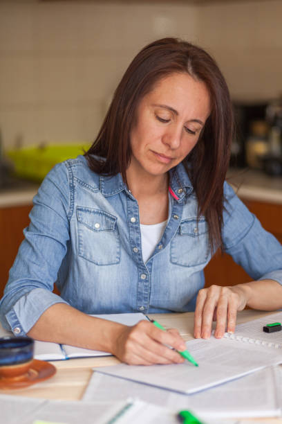 istock Mid adult woman reading a text from a textbook while studying at home. 1284052800