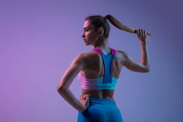 giovane donna sportiva che si allena isolata su uno sfondo di studio sfumato alla luce al neon. atletico e aggraziato - fitness apparel foto e immagini stock