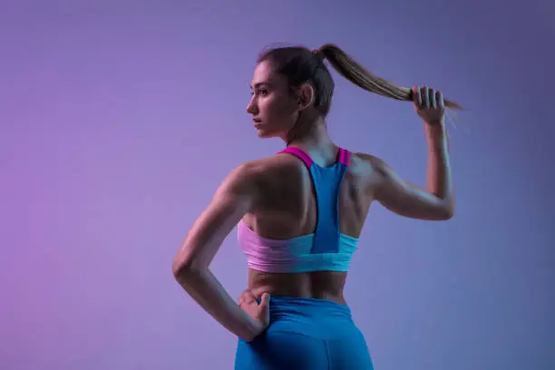 Strong. Young sportive woman training isolated on gradient studio background in neon light. Athletic and graceful. Modern sport, action, motion, youth concept. Beautiful caucasian woman practicing.