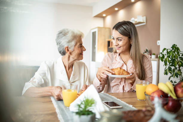 A cheerful young girl serves breakfast to her grandmother at home Cheerful young girl serving breakfast to an elderly woman at home - A social worker visiting an elderly woman teenage girl with grandmother stock pictures, royalty-free photos & images
