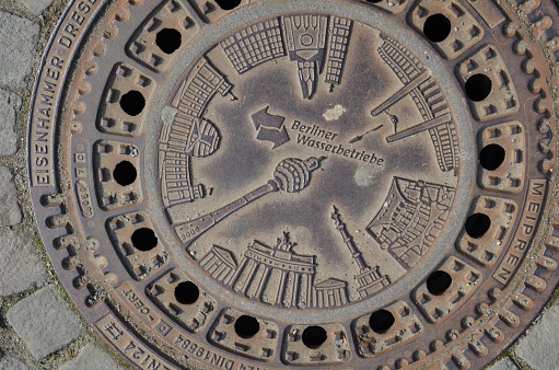 Berlin, March 29, 2014 - Sewer cover of the Berliner Wasserbetriebe in Berlin with the principal buildings of the city.
