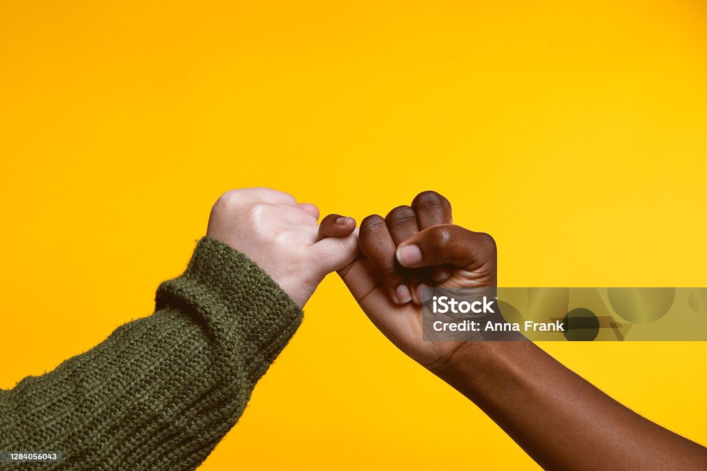 I pinky promise Studio shot of two young women linking their fingers against a yellow background Pinky Promise Stock Photo