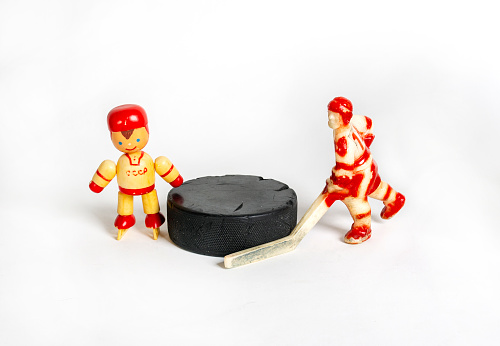 Hockey. Two red toy hockey players stand next to the puck. Children's hockey, a symbol of sports hockey. Isolated on a white background.