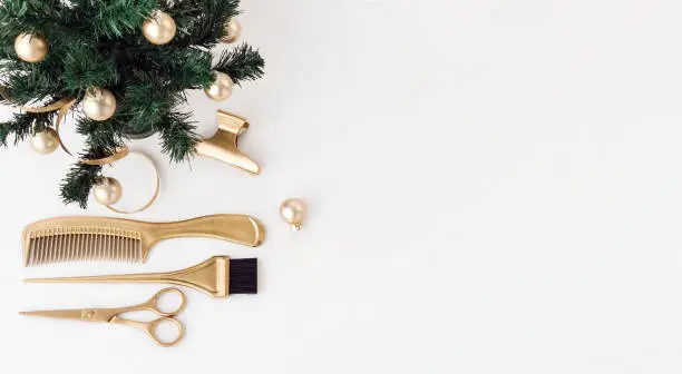 Photo of Banner with hairdressing tools in gold color and a Christmas tree on a white background. Holiday template with hair salon accessories with space for text.