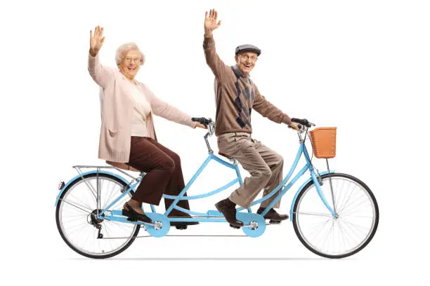 Photo of Elderly couple riding a blue tandem bicycle and waving