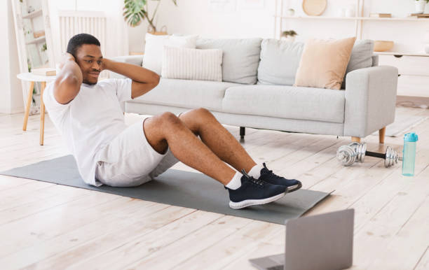 homem africano exercitando-se fazendo abdominais sentados no laptop dentro de casa - sit ups - fotografias e filmes do acervo