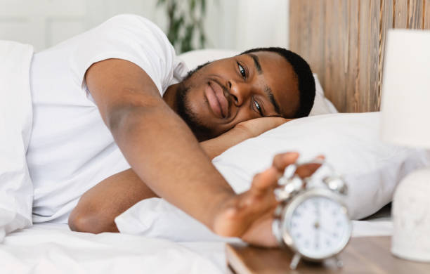 Wellslept Black Man Turning Off Alarm-Clock Waking Up In Bedroom Good Morning. Wellslept Black Man Turning Off Alarm Clock Waking Up Lying In Bed In Modern Bedroom At Home. Early Awakening, Time To Get Up Concept. Selective Focus person waking up stock pictures, royalty-free photos & images