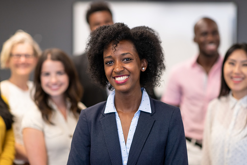 An African American woman wearing a business suit smiles at the forefront of a group of businesspeople.