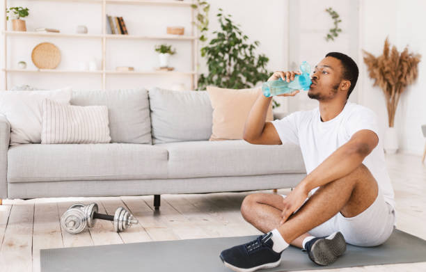 istock Black Man Drinking Water During Workout Sitting On Mat Indoors 1284070514
