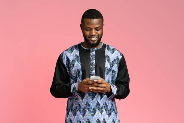 istock Smiling black guy using smartphone, wearing african t-shirt 1284070685
