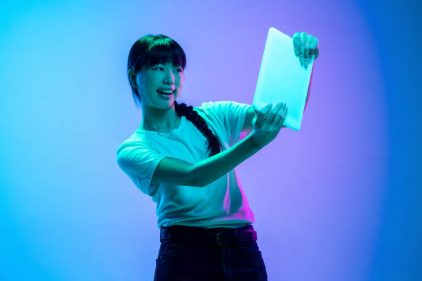 istock Young asian woman's portrait on gradient blue-purple studio background in neon light 1284071088