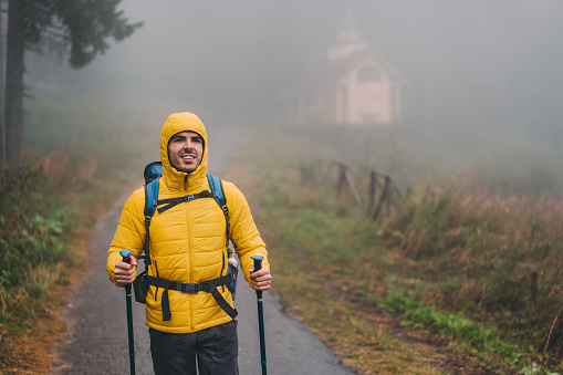 Tourist with nordic walking poles is hiking at rainy day