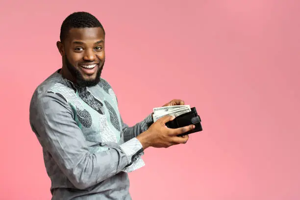 Photo of Excited african-american man putting money into wallet