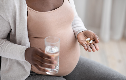 Prenatal Vitamins And Supplements. Unrecognizable black pregnant woman taking pills capsules and glass of water, using medicaments for healthy pregnancy, cropped image, closeup