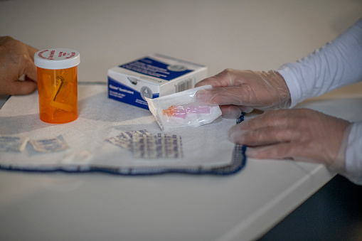 A nurse visits her elderly patient in her home and dispenses her medication on the kitchen counter.
