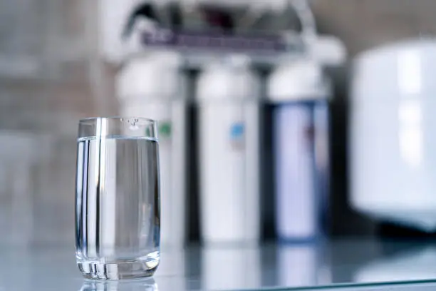 Photo of Pure water in glass and water filters on the blurred background. Household filtration system.
