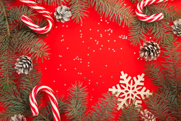 istock Christmas tree branches, candy canes, snowflake and pine cones on red background with silver confetti stars. Copy space. 1284079083