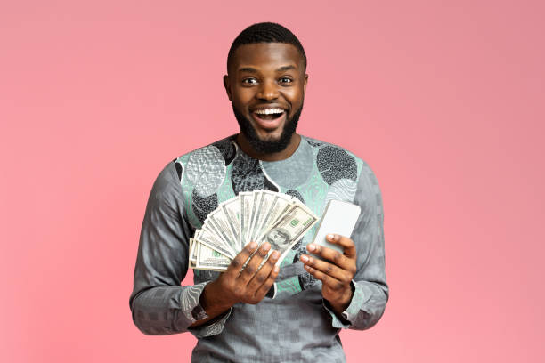istock Happy black guy holding cash and mobile phone 1284079330