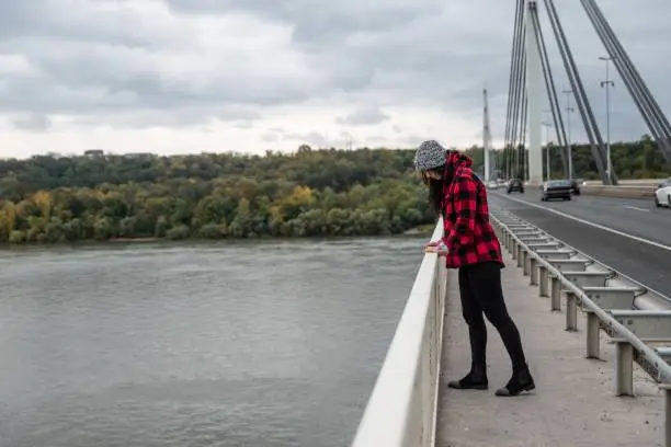 Young depressed homeless girl or woman standing alone on the bridge want to jump in to the water of the river and to commit suicide after hard life on the street selective focus