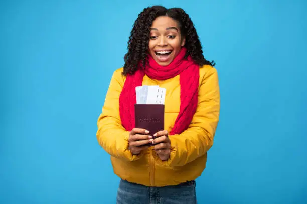 Excited African American Traveler Lady Holding Boarding-Pass Tickets Standing In Studio Over Blue Background. Vacation Finally, Winter Travel And Tourism Concept