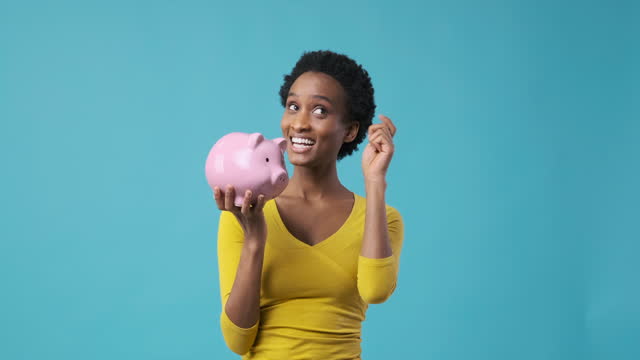 Happy woman inserting coin into piggy bank