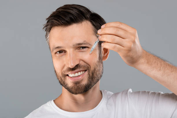 Middle-aged handsome man applying anti-aging face serum Middle-aged handsome man applying anti-aging serum and smiling at camera over gray studio background, empty space. Handsome cheerful man using nourishing serum for his face, closeup blood serum photos stock pictures, royalty-free photos & images