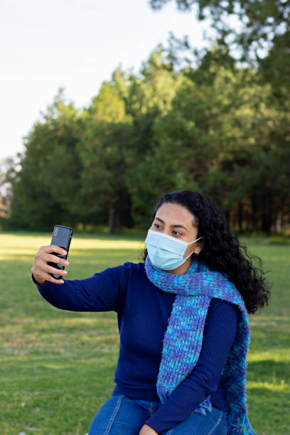 istock young woman wearing mask, taking a selfie in a park 1284086984