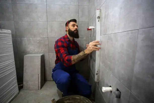 Construction worker on a construction site of a new bathroom, measuring with a level. About 30 years old, Caucasian male.