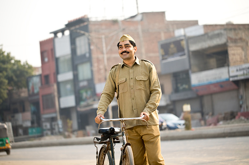 Male postal worker in uniform holding bicycle handlebar on street