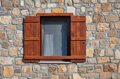 Window with brown wooden shutter on a stone wall