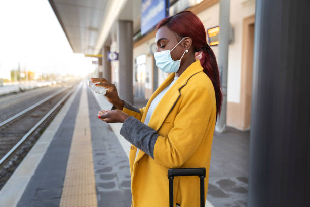 istock Woman using hand sanitizer while waiting the train on the station platform 1284092974