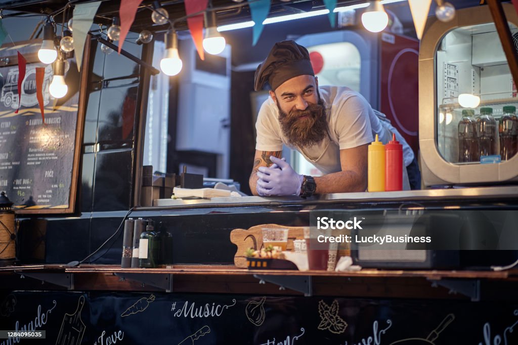 male employee in fast food service waiting for customers leaned on desk young male employee in fast food service waiting for customers leaned on desk Food Truck Stock Photo