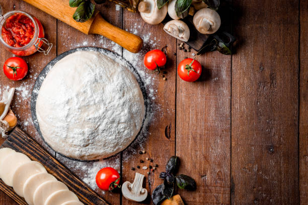 istock Ingredients for making pizza - dough, mozzarella cheese, tomatoes, mushrooms and basil on a wooden background. Top view, free space for text 1284095424