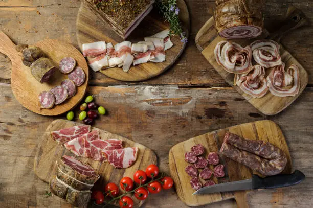Platters of artisanal cold cuts on ancient wooden table, with salami, capocollo, bacon, lard and sausage.