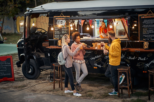 group of young people socializing while eating outdoor in front of modified truck for fast food