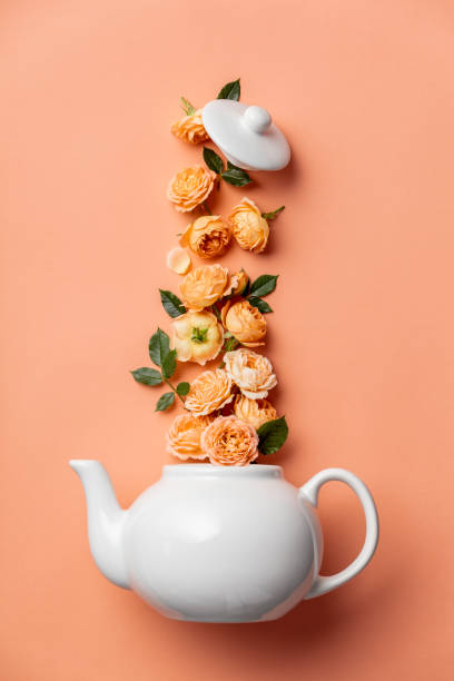istock Creative layout made of whte tea pot with orange roses on pink background 1284096624