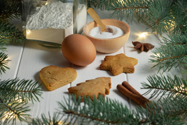 istock Gingerbread, flour, egg, sugar, anise next to branches of a Christmas tree with light bulbs on a white wooden background 1284097860