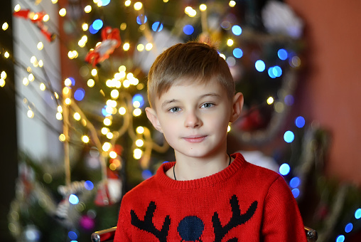 portrait of a handsome blond boy with bright eyes in a Christmas sweater on a background of bokeh lights