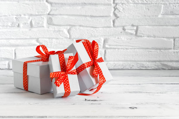 istock Three of gift boxes with red ribbon on a white wooden table, brick backdrop. Selective focus, copy space 1284099893
