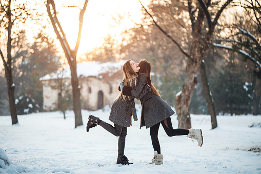 Two young Caucasian beautiful women embracing in the snow and having fun.