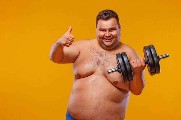 istock Fat man doing workout traning with dumbbells. Happy guy isolated over yellow background. 1284101940