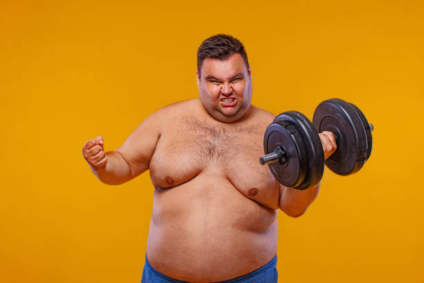 istock Fat man doing workout traning with dumbbells. Happy guy isolated over yellow background. 1284101946