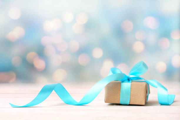 Christmas gift,craft box with blue ribbon on wooden white table blurred lights background empty space.New year backdrop. Christmas gift,craft box with blue ribbon on wooden white table blurred lights background empty space. gift lounge stock pictures, royalty-free photos & images