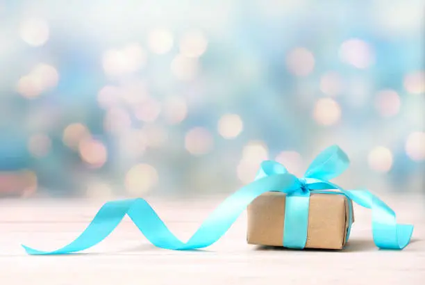 Christmas gift,craft box with blue ribbon on wooden white table blurred lights background empty space.