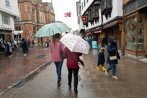 Canterbury, UK - Oct 29 2020 Shoppers dress for the heavy rain and carry umbrellas on the pedestrian parade.