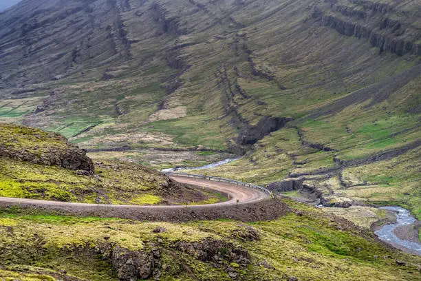 Ring road on route 1 in southeast Iceland highway with moss green landscape mountains and car on steep slope with overcast cloudy stormy weather in Berufjordur area