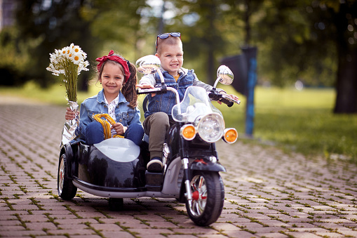 Happy little boy and girl driving in a toy motorcycle in the park