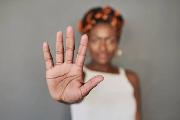 Studio portrait of a young woman holding her palm out against a grey background