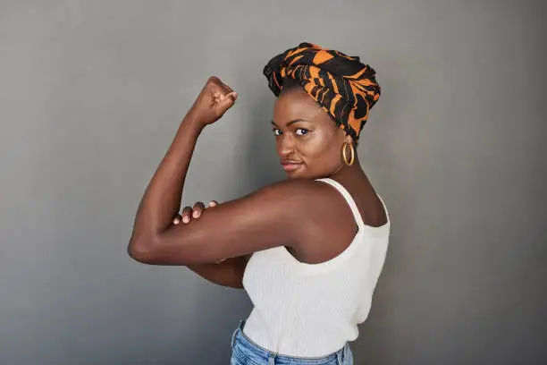 Studio portrait of a young woman flexing her biceps against a grey background
